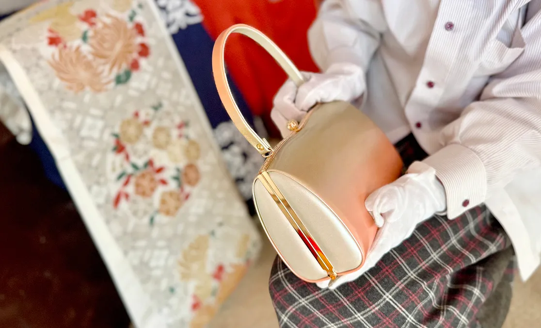 和柄の敷物の上で、小さなハンドバッグを両手で持ち上げている人物の様子