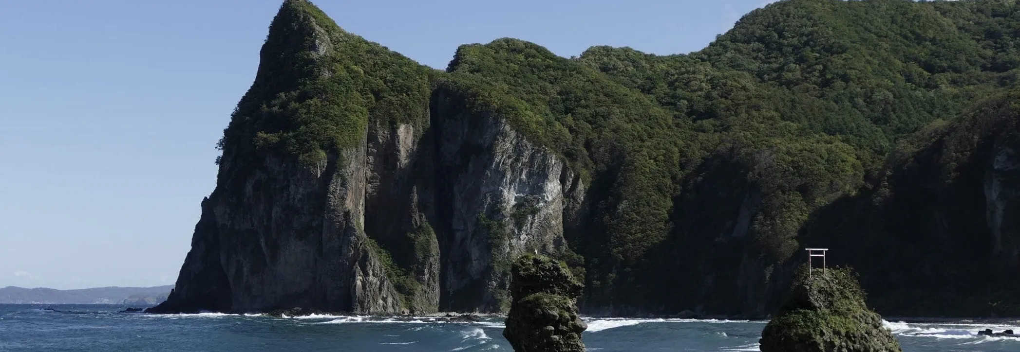 海に面した断崖と岩礁が連なる風景で、晴天の下で穏やかな海が広がっている様子